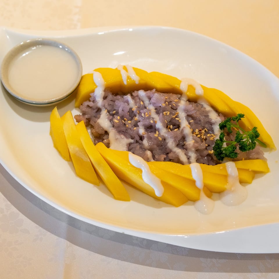 Purple sticky rice with fresh mango slices, coconut milk drizzle, sesame seeds, and parsley garnish.