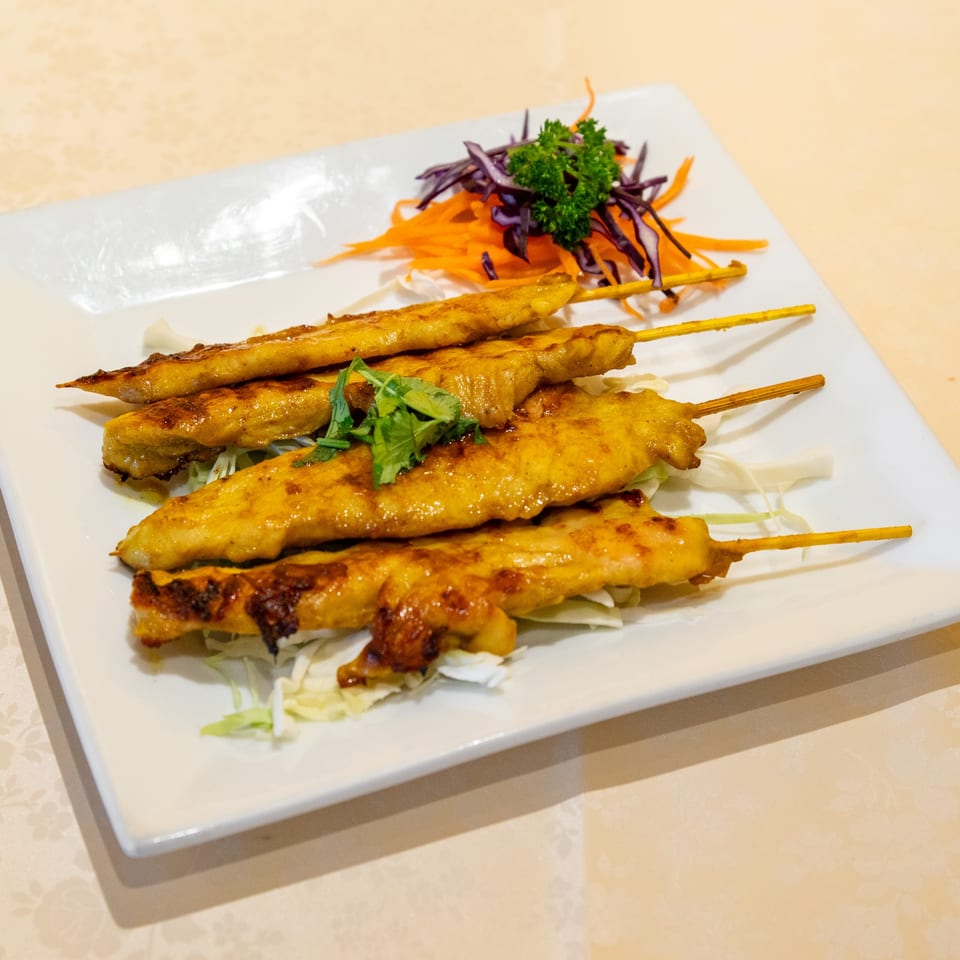 Golden chicken satay skewers with fresh herbs, shredded carrots, and purple cabbage on a white plate.