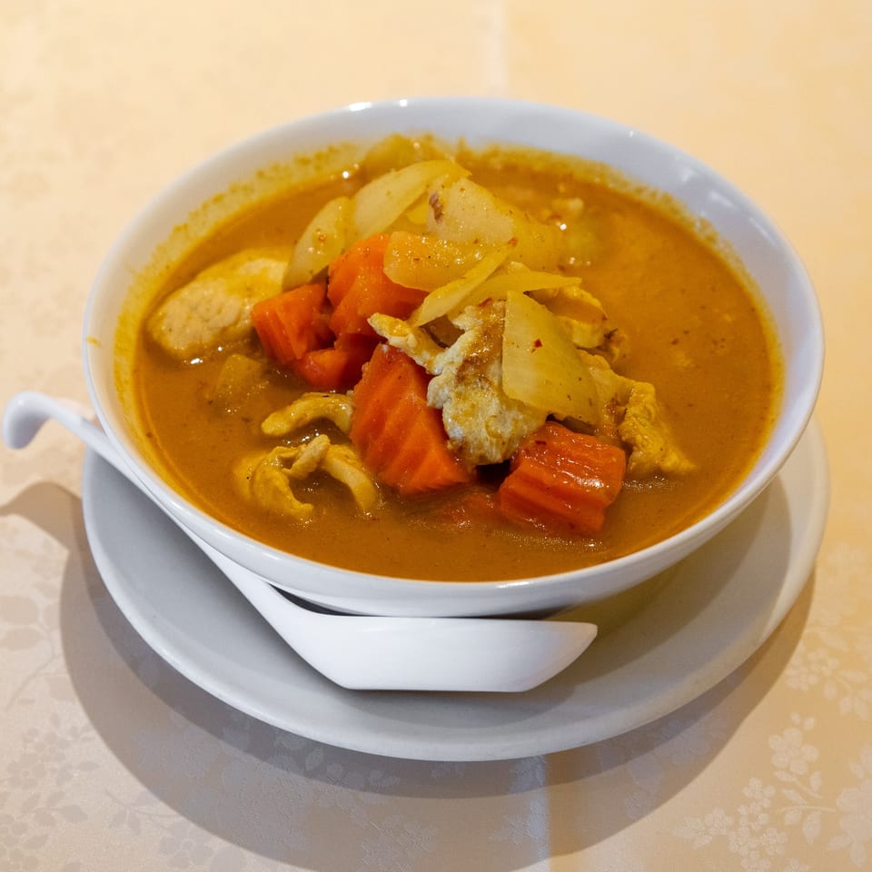 A bowl of Thai yellow curry with chicken, carrots, and onions, served on a white plate.