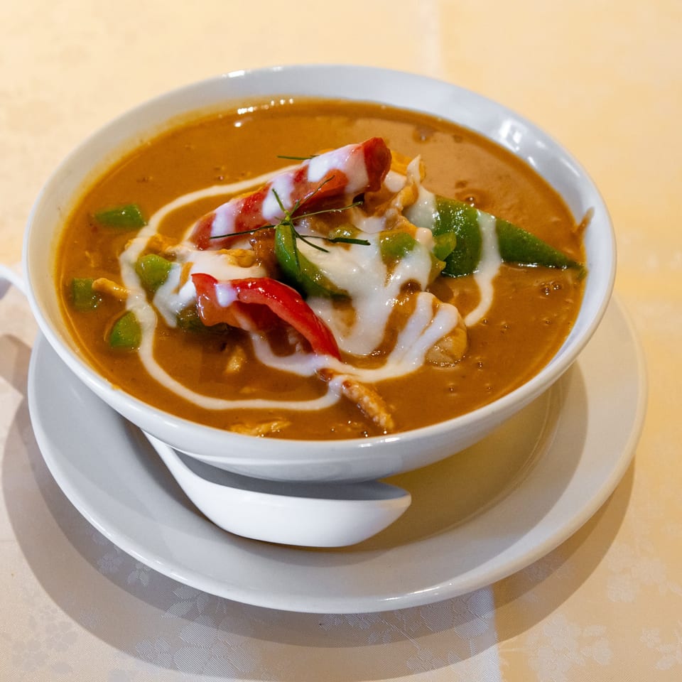 A bowl of Thai red curry with chicken, bell peppers, and coconut milk drizzle.