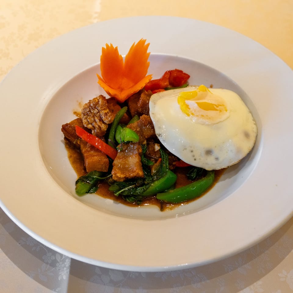 Thai basil pork with a fried egg and carved carrot garnish on a white plate.