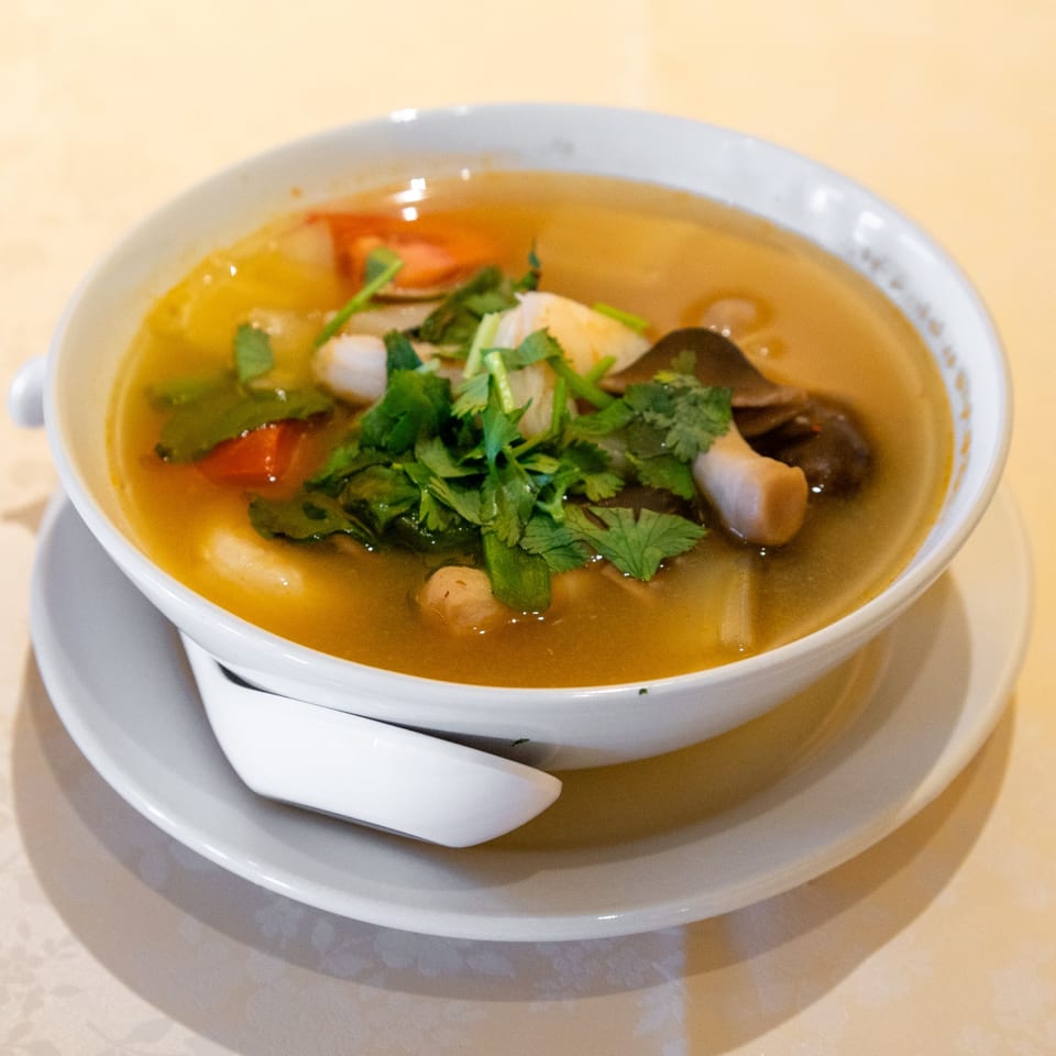 A bowl of ThaiTom Yum soup with shrimp, mushrooms, and cilantro on a white plate.